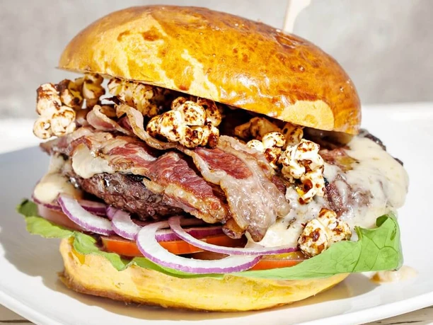 Die fette Kuh Burger A burger with bacon, popcorn, onions, salad and a patty.