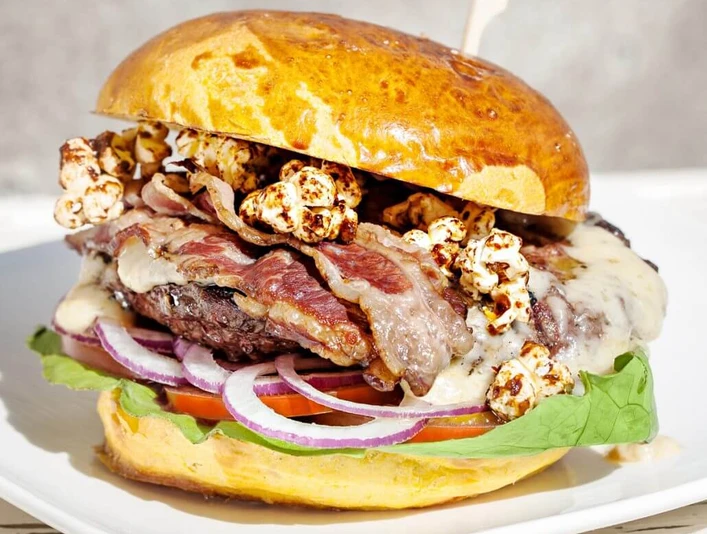 Die fette Kuh Burger Üppig belegter Burger mit Speck, Popcorn, Zwiebel, Salat und Patty.A burger with bacon, popcorn, onions, salad and a patty.