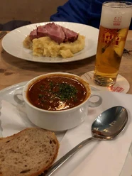 Brauhaus Pütz Ein köstliches Gericht aus herzhaftem Gulasch und Brot, begleitet von einem erfrischenden Bier.