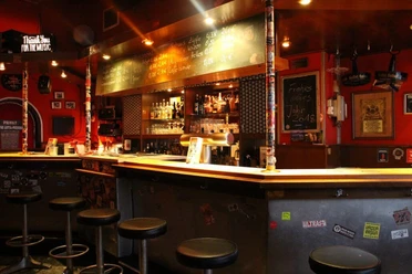 Lotta Bar Innenansicht auf den Barbereich. Die Theke ist schwarz lackiert und davor stehen Metallhocker.