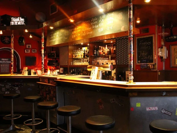 Lotta Bar Interior view of the bar area. The counter is painted black and metal stools are placed in front of it.