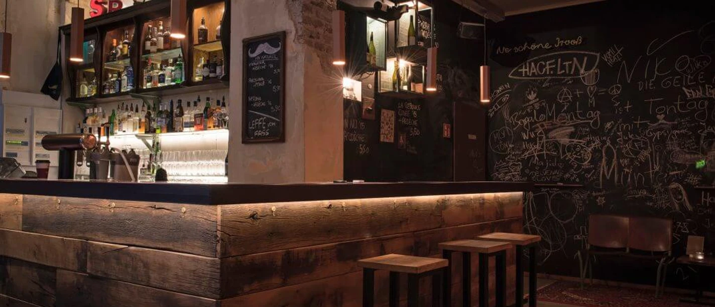 Bar em Schnörres Wood-paneled bar with stools in dim light. A chalkboard adorns the entire back wall with scribbles on it.