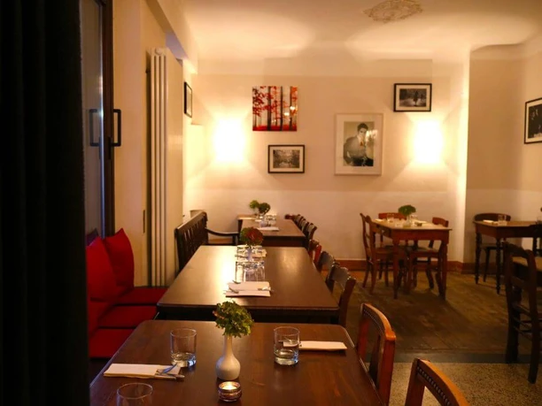 Traubenzeit A tastefully decorated room featuring wooden tables and chairs, complemented by decorative artwork adorning the walls.