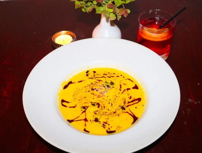 Traubenzeit Ein weißer Teller auf dunklem Tisch, gefüllt mit cremiger Suppe, dekoriert mit Ölspiralen und Samen.A white plate placed on a dark table, filled with creamy soup decorated with spirals of oil and sprinkled with seeds.