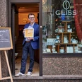 Michael Glisss Ein Mann steht mit einer Auszeichnung vor dem Café „GLISS“A man stands with an award in front of the "GLISS" café