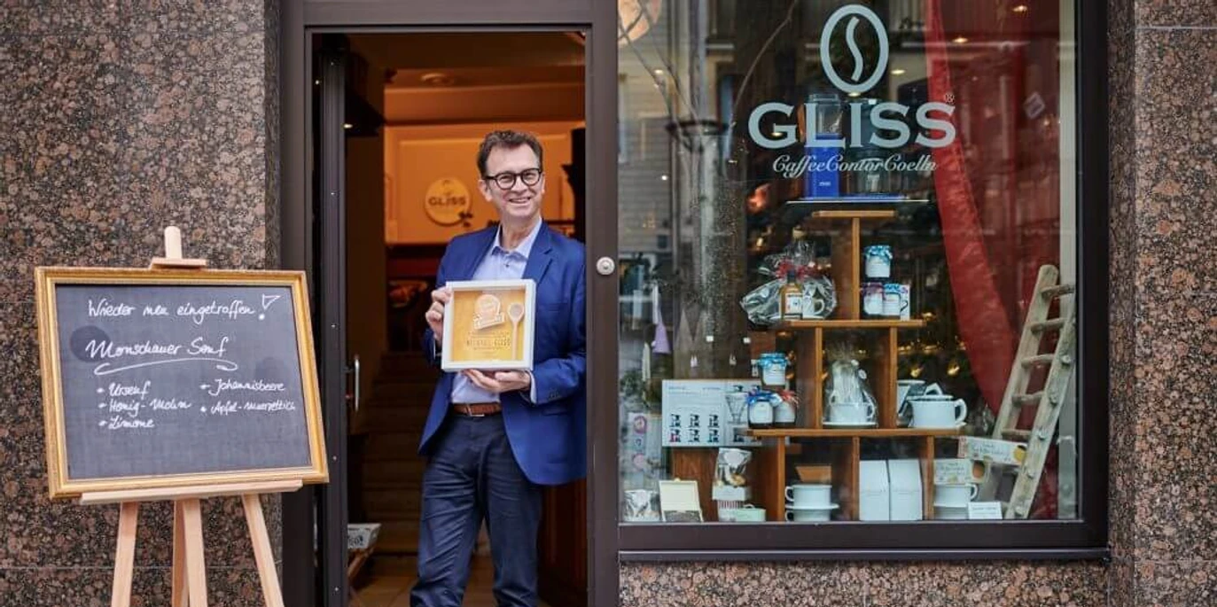 Michael Glisss Ein Mann steht mit einer Auszeichnung vor dem Café „GLISS“A man stands with an award in front of the "GLISS" café