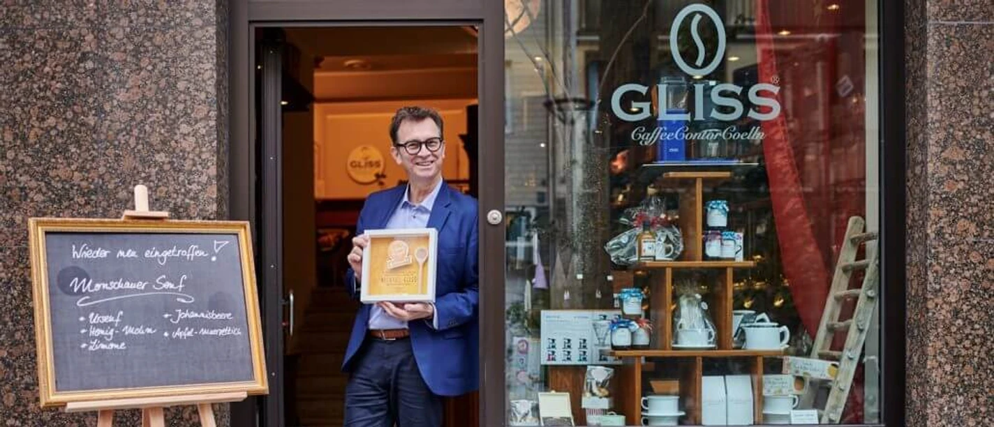 Michael Glisss Ein Mann steht mit einer Auszeichnung vor dem Café „GLISS“