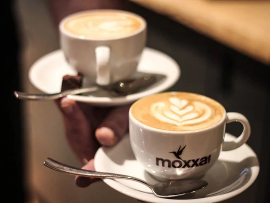 moxxa cafe die Rösterei Zwei Cappuccinos auf Untertassen mit Löffeln, serviert in weißen Moxxa-Tassen.Two cappuccinos on saucers with spoons, served in white Moxxa cups.