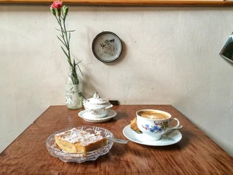 Leuchte coffee bar There is a cup of coffee and a plate of almond cake on a wooden table. The tableware is porcelain and decorated with flowers.