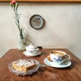 Leuchte coffee bar Auf einem Holztisch stehen eine Tasse Kaffee und ein Teller mit Mandelkuchen. Das Geschirr ist aus Porzellan und floral verziert.There is a cup of coffee and a plate of almond cake on a wooden table. The tableware is porcelain and decorated with flowers.