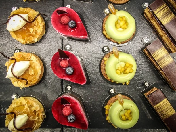 Törtchen Törtchen An assortment of artistically decorated tartlets presented on a slate platter, each uniquely garnished.