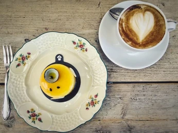 Törtchen Törtchen Ein elegantes gelbes Törtchen auf feinem Porzellanteller neben einer Cappuccinotasse mit Herzmotiv.An elegant yellow tartlet served on a fine porcelain plate next to a cappuccino cup decorated with a heart motif.