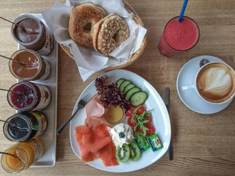 CafeCafe Frühstückstisch mit Bagels, Aufschnitt, Cappuccino und Fruchtsaft.