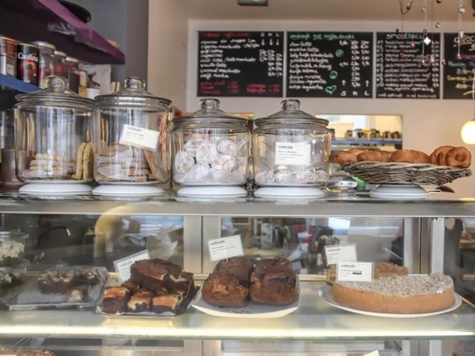 CafeCafe Vitrine mit Kuchen und Glasgefäße gefüllt mit Keksen. Im Hintergrund hängen Kreidetafeln an der Wand mit angebotenem Menü.Showcase with cakes and glass jars filled with biscuits. In the background, chalkboards with the menu are hanging on the wall.