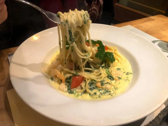 Toscanini Ein Teller Spaghetti in cremiger Soße mit Garnelen, Tomatenstücken und Petersilie auf Holzuntergrund.A plate of spaghetti in a creamy sauce with shrimp, tomato pieces, and parsley, served on a wooden surface.