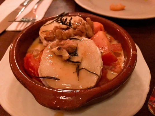 Tapeo and co Eine rustikale Tonschale gefüllt mit überbackenem Ziegenkäse, Tomaten, Walnüssen und Rosmarin.A rustic clay bowl filled with baked goat cheese, tomatoes, walnuts, and rosemary.