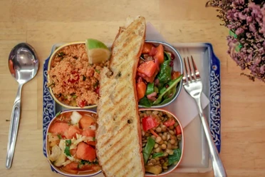 Eine bunte Salat-Auswahl mit Quinoa, Linsen, Tomaten, Limette und getoastetem Brot auf einem blau verzierten Teller.