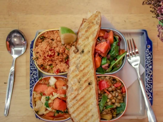 Veedel Vital Eine bunte Salat-Auswahl mit Quinoa, Linsen, Tomaten, Limette und getoastetem Brot auf einem blau verzierten Teller.A colorful salad assortment featuring quinoa, lentils, tomatoes, lime, and toasted bread, served on a blue decorated plate.