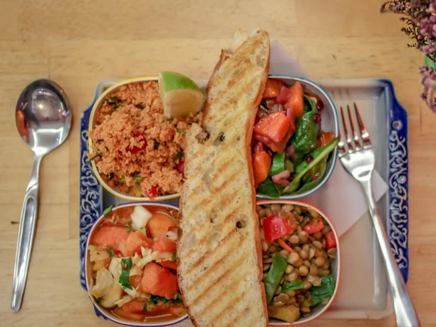 Veedel Vital Eine bunte Salat-Auswahl mit Quinoa, Linsen, Tomaten, Limette und getoastetem Brot auf einem blau verzierten Teller.