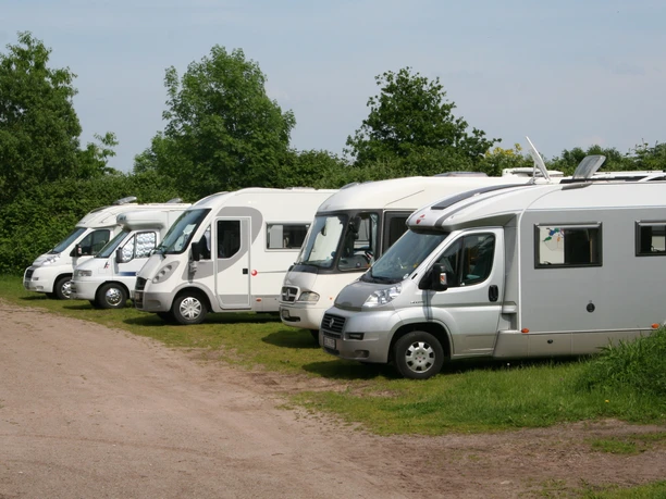 RV's are parked on a grassy site next to a castle surrounded by greenery.