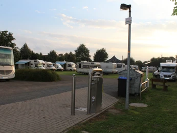Wohnmobilstellplatz Bruchhausen-Vilsen Wohnmobilstellplatz in einer grünen Umgebung mit mehreren Reisemobilen, gepflasterten Wegen und Laterne.