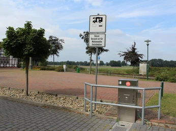 Reisemobilstellplatz mit gepflasterter Fläche, Stromanschluss und Hinweisschild im ländlichen Lavelsloh.