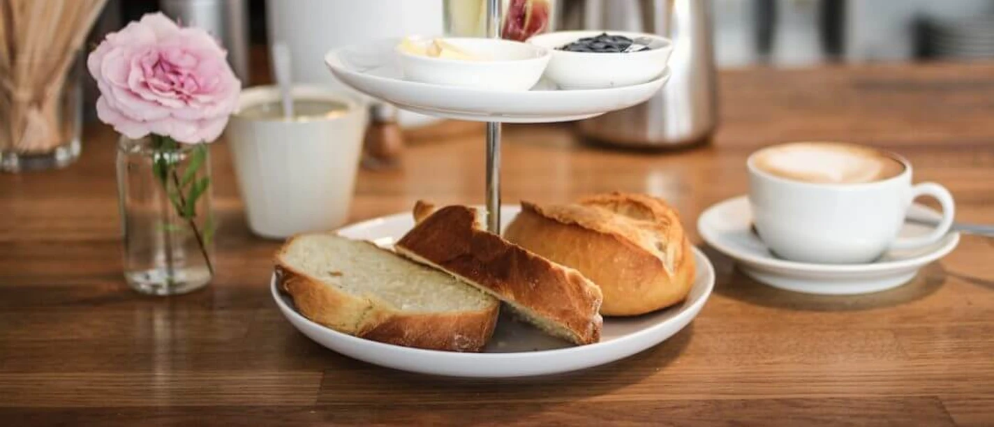 Cafe dein und mein Ein köstliches Frühstücksset mit frisch gebackenen Brötchen, Butter, Marmelade, Obst und Kaffee.