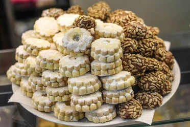 Simitzade Vielzahl von feinen Gebäckstücken, darunter mit Puderzucker bestäubte Kekse und mit Samen bedeckte Cookies auf einem Teller angerichtet.