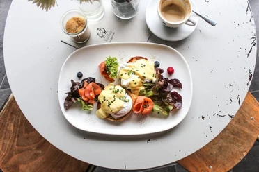 Hinz und Kunz Frühstücksteller mit Egg Benedict, Lachs, Salat und einem schwarzen Kaffee.