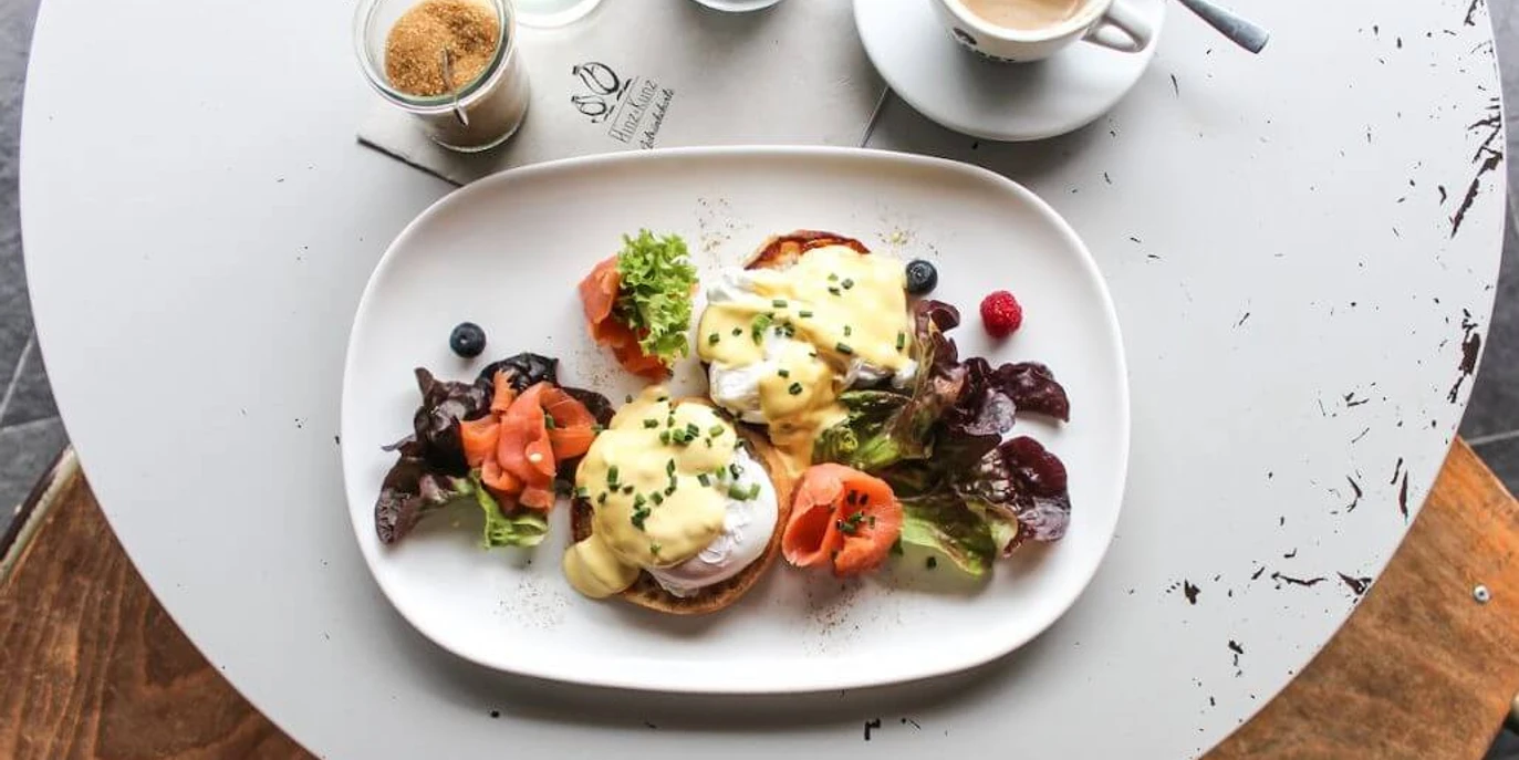 Hinz und Kunz Frühstücksteller mit Egg Benedict, Lachs, Salat und einem schwarzen Kaffee. Breakfast plate with egg benedict, salmon, salad and a black coffee.