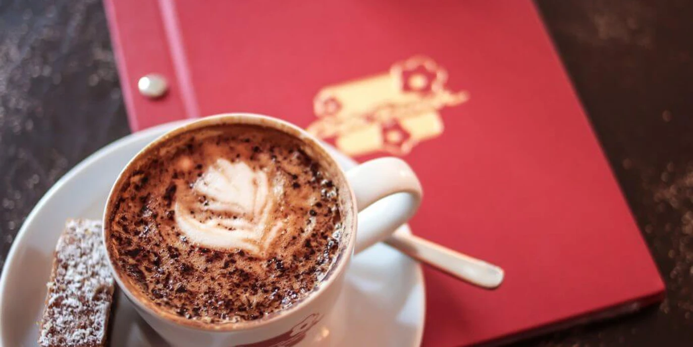 Café Franck Eine Tasse Cappuccino mit Schaumkunst, serviert auf einer weißen UntertasseA cup of cappuccino with foam art, served on a white saucer