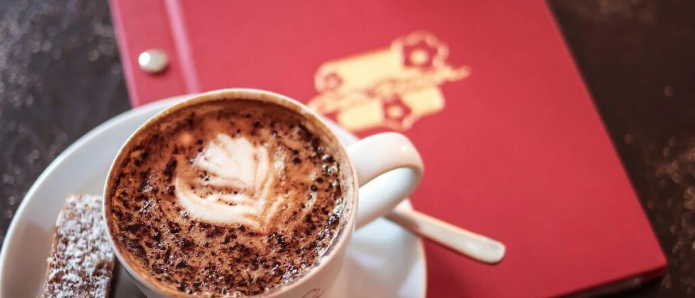 Café Franck A cup of cappuccino with foam art, served on a white saucer