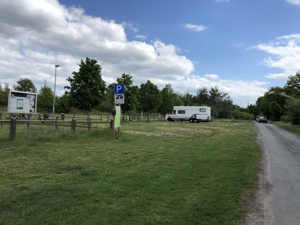 Leese WoMo Platz Grüner Wohnmobilstellplatz in ländlicher Umgebung mit Parkschildern und Fahrzeug unter blauem Himmel.