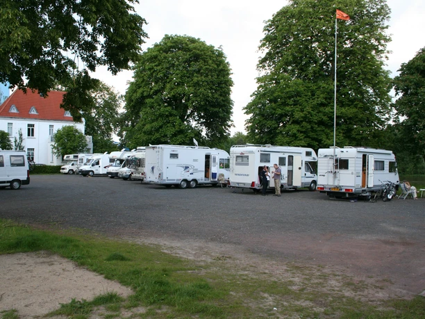 A RV parking area with several parked RVs on a paved surface, surrounded by trees.