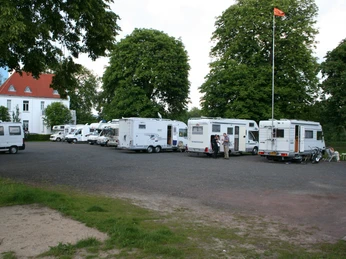 Wohnmobilstellplatz Nienburg Wohnmobilstellplatz mit mehreren geparkten Wohnmobilen auf einem asphaltierten Bereich, umgeben von Bäumen.