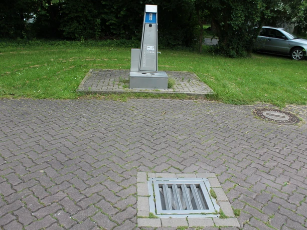 Stellplatz in Rodewald mit Stromsäule und Entsorgungsstation auf gepflastertem Gelände, umgeben von Bäumen.