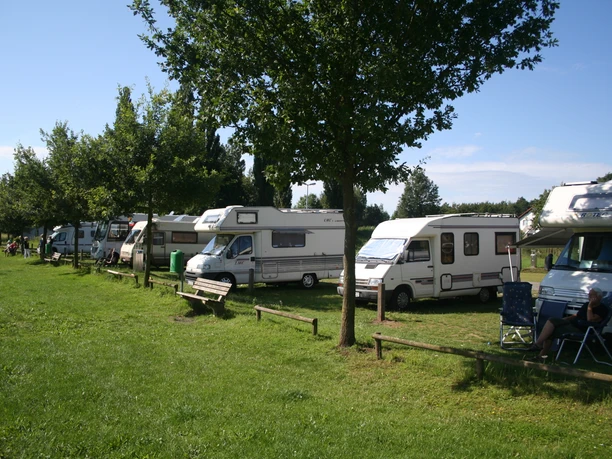 Wohnmobilstellplatz Stolzenau Wohnmobilstellplatz mit mehreren Wohnmobilen, schattenspendenden Bäumen und gepflegter Rasenfläche.