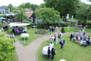 Nienburger Spargelfest Mensen genieten van een openlucht aspergefestival met kraampjes en tafels, omgeven door groene natuur.