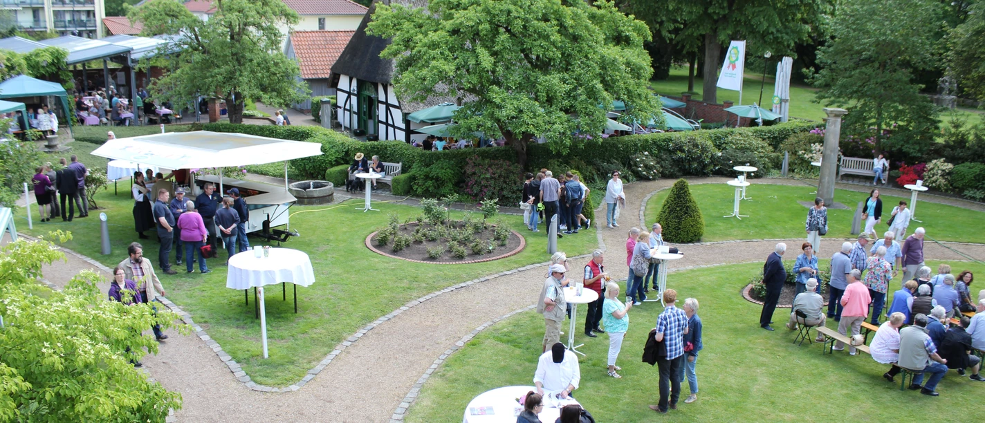 Nienburger Spargelfest People enjoy an outdoor asparagus festival with stalls and tables, surrounded by green nature.