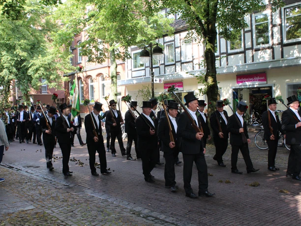 Ausmarsch Scheibenschießen Nienburg Eine Gruppe festlich gekleideter Männer, die in einem traditionellen Umzug eine Kopfsteinpflasterstraße entlang marschiert.