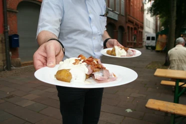 One person holds a platter of jacket potatoes, matjes, ham and a generous portion of cream sauce.
