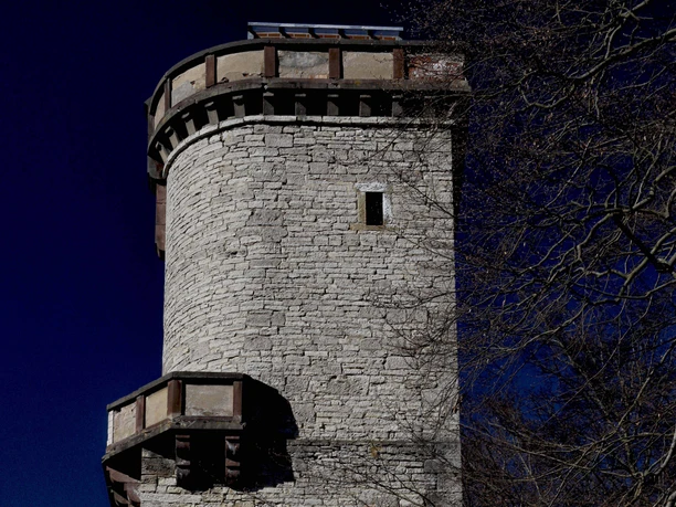 Kaiser-Friedrich-Turm (Altendorfer Berg)_Außenansicht Runder Aussichtsturm aus hellem Stein mit Zinnenkranz im Einbecker Stadtwald vor tiefblauem Himmel