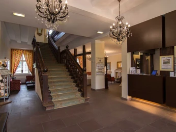 Großer Eingangsbereich mit luxuriösen Kronleuchtern, Empfangstresen und einer breiten Holztreppe.