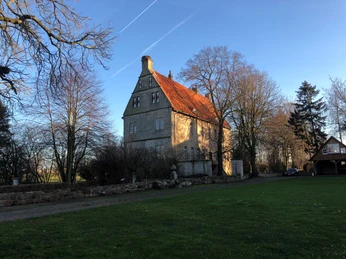 Burg Schlüsselburg Burg Schlüsselburg im Sonnenuntergang, von Bäumen umgeben, mit markantem rotem Dach vor blauem Himmel.
