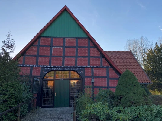 Katholische Kirche Windheim Ein traditionelles Fachwerkhaus mit rotem Ziegeldach und grünem Gartentor, umgeben von Bäumen.