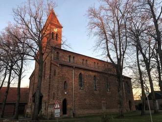 Kirche Friedewalde Backsteinkirche aus dem 19. Jahrhundert mit hohem Turm, umgeben von kahlen Winterbäumen.