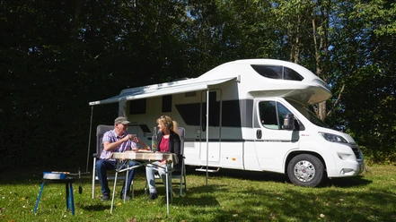 Wohnmobilhafen in Brakel-Bellersen Zwei Personen sitzen im Freien vor einem geparkten Wohnmobil und genießen gemeinsam eine Mahlzeit.