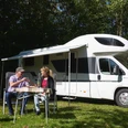 Wohnmobilhafen in Brakel-Bellersen Zwei Personen sitzen im Freien vor einem geparkten Wohnmobil und genießen gemeinsam eine Mahlzeit.