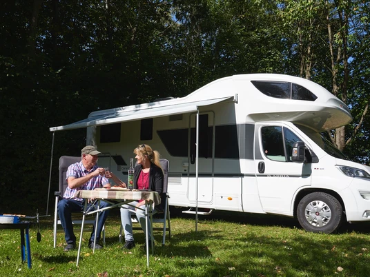 Wohnmobilhafen in Brakel-Bellersen Zwei Personen sitzen im Freien vor einem geparkten Wohnmobil und genießen gemeinsam eine Mahlzeit.
