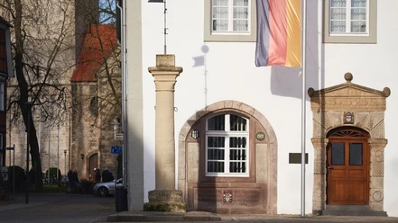 Die Rolandsäule steht auf einem Marktplatz vor einem historischen Gebäude mit deutscher Flagge.